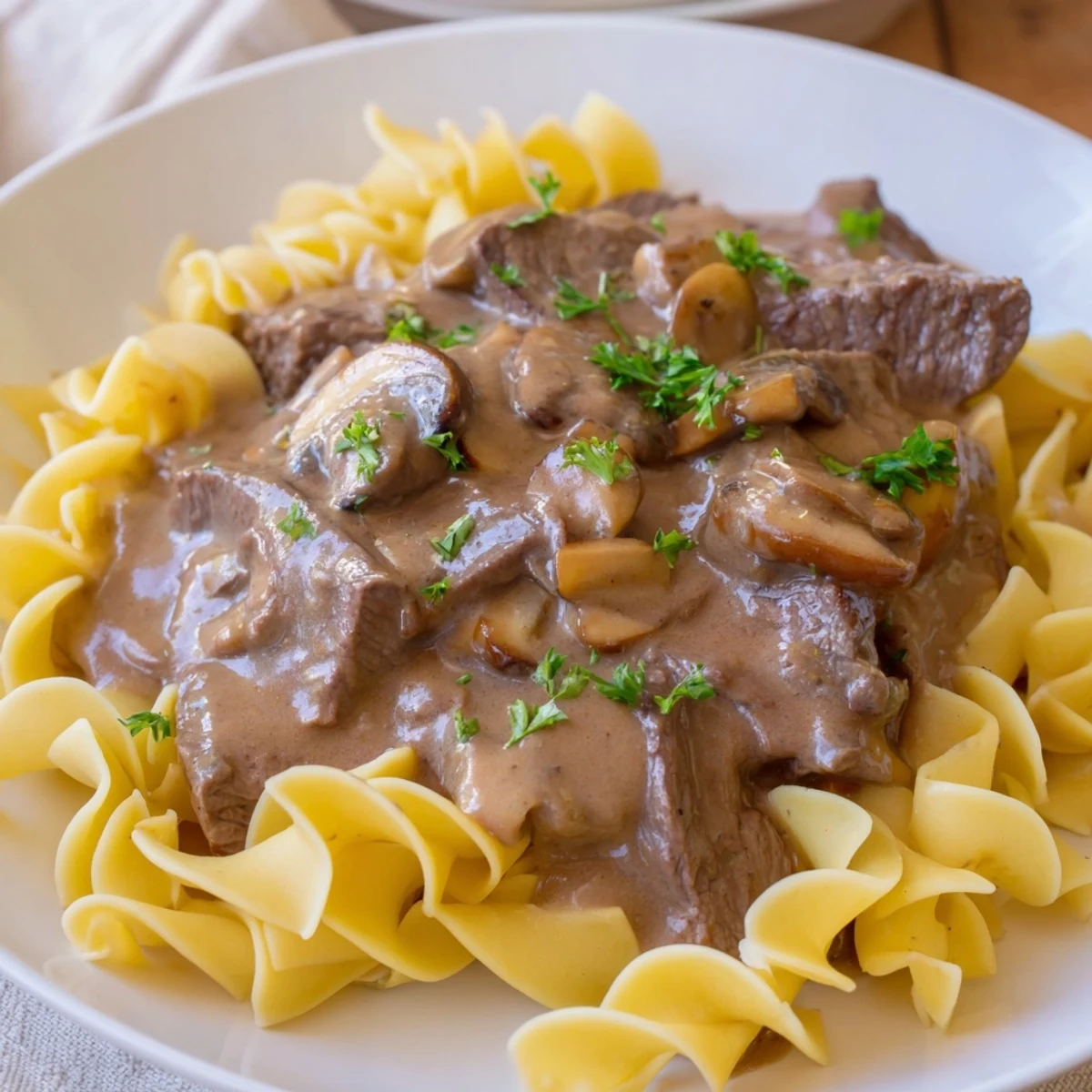 Steaming beef stroganoff with mushroom gravy, served atop tender egg noodles, ready to be enjoyed.