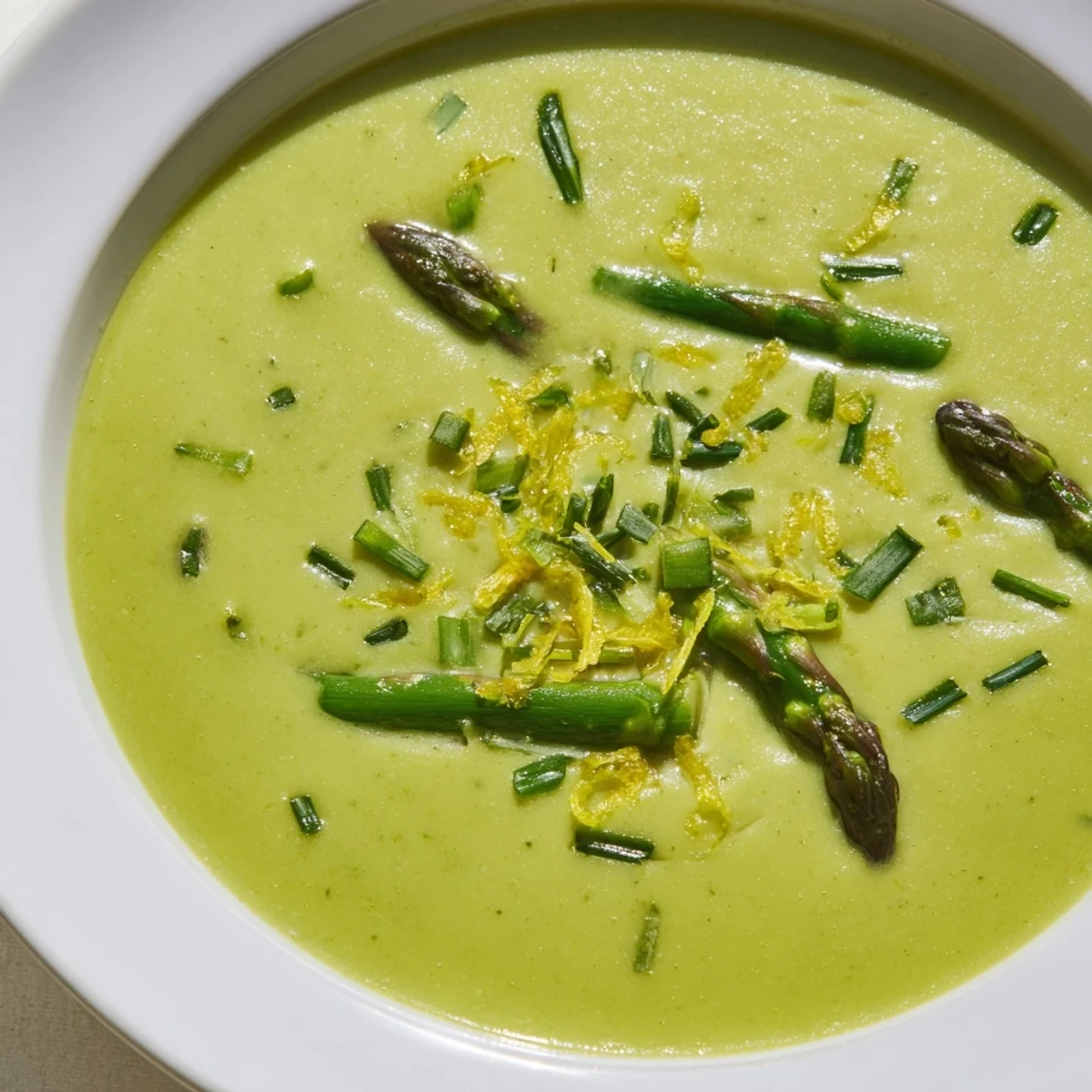 Vibrant green creamy asparagus soup topped with herbs, perfect for a cozy lunch.