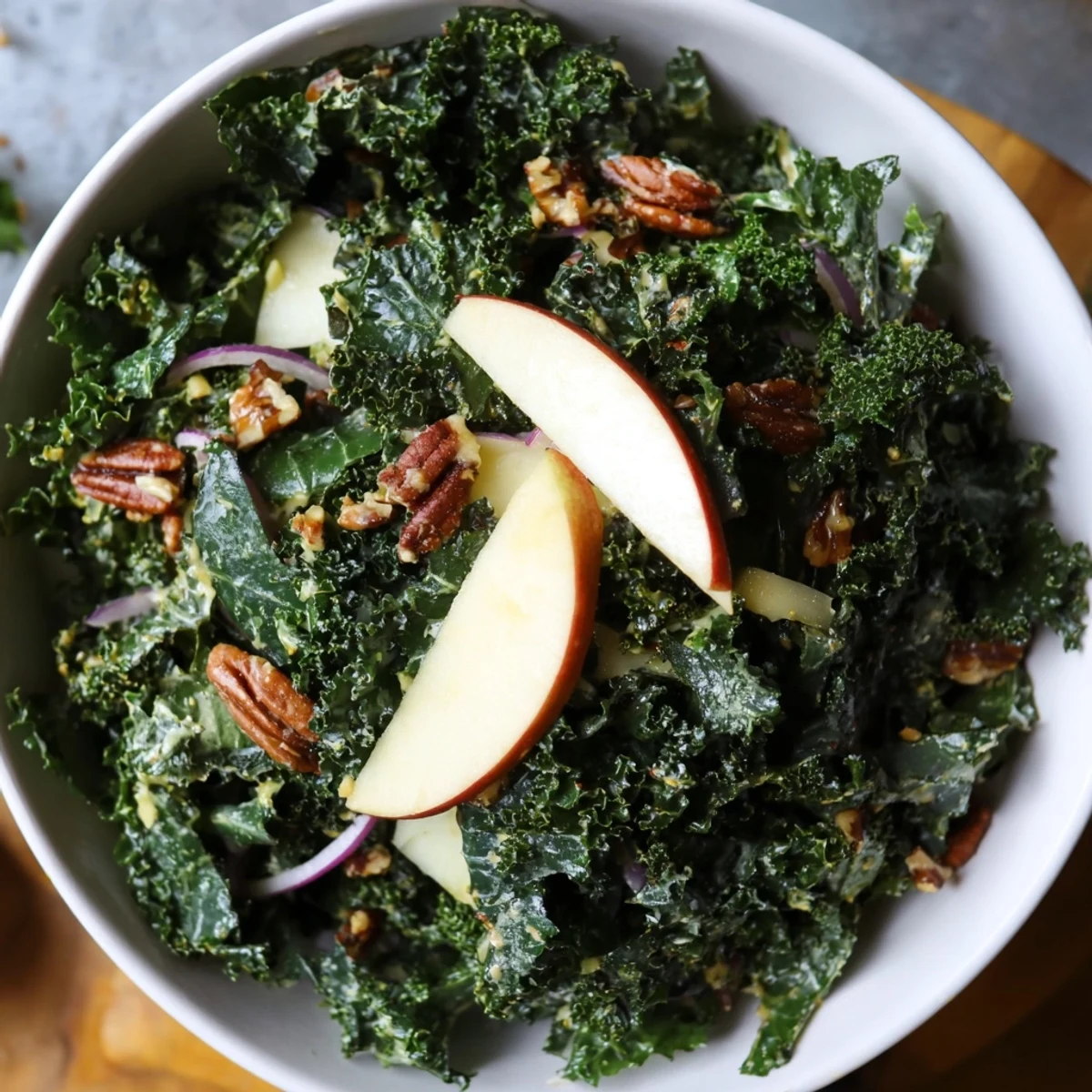 Close-up view of a fresh serving of Winter Kale Salad with Apple and Sharp Cheddar, highlighting the texture of chopped kale, apple wedges, and toasted nuts on a rustic wooden table.