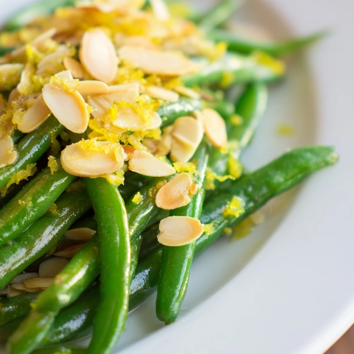 Garlic sautéed green beans topped with toasted almonds and fresh lemon zest in a serving bowl.