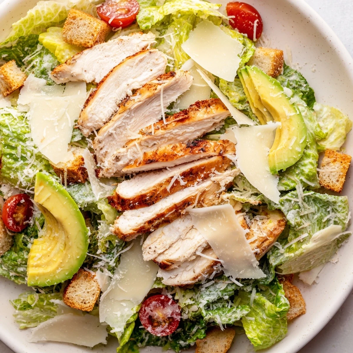 Close-up of Chicken Caesar Salad with Avocado featuring juicy chicken, grated Parmesan, and a drizzle of tangy homemade dressing.