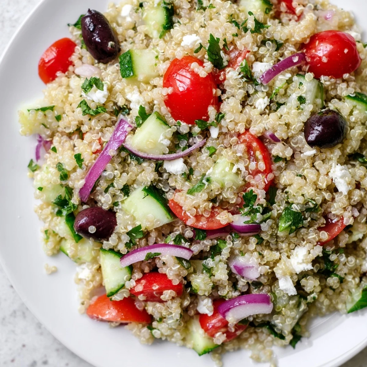 Bright Mediterranean Quinoa Salad with tomatoes, cucumbers, olives, and feta in a white bowl.