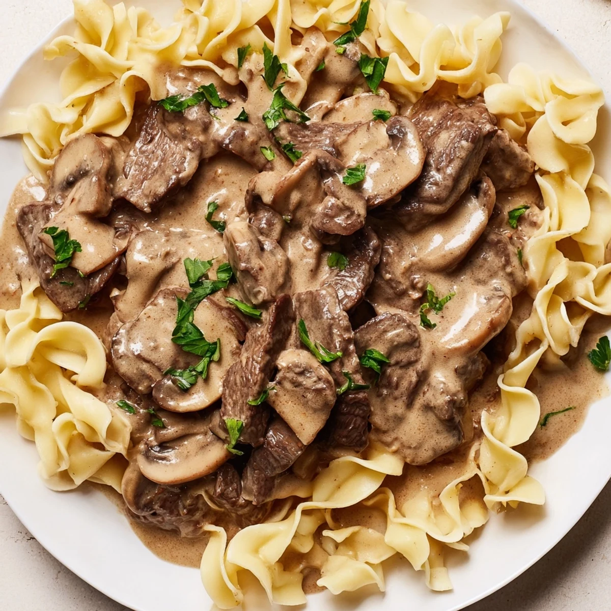 Savory Beef Stroganoff with Mushroom Gravy ladled over glossy egg noodles, garnished with fresh parsley.