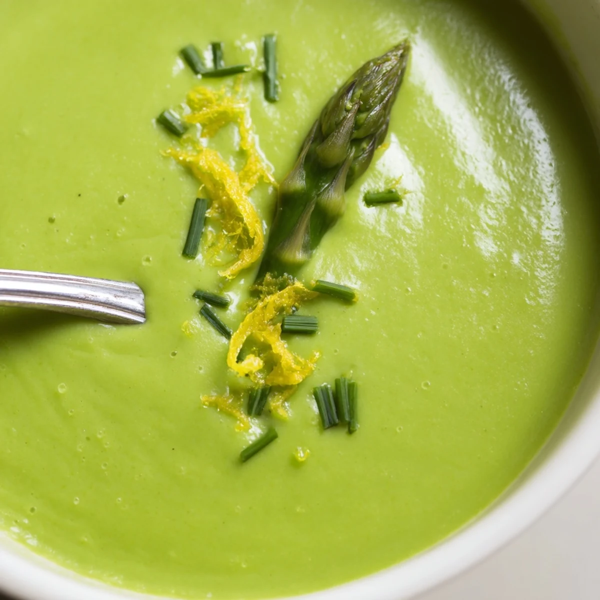 Silky, vibrant green Creamy Asparagus Soup with Lemon steaming gently beside a lemon wedge and sliced artisan bread for dipping.