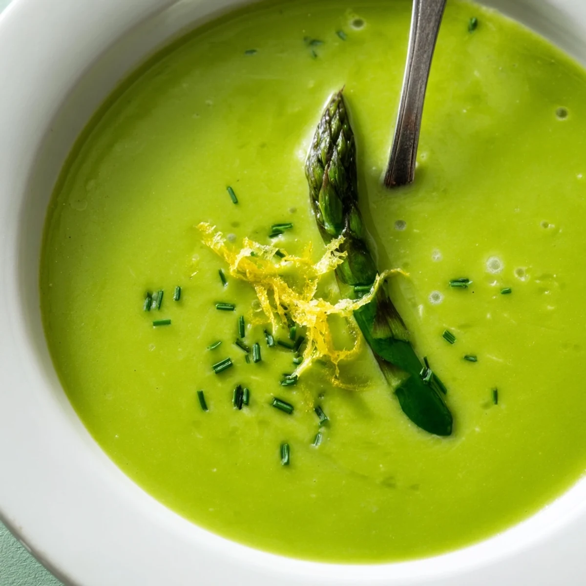 A single bowl of Creamy Asparagus Soup with Lemon garnished with dill, showing its smooth, velvety texture against a bright backdrop.