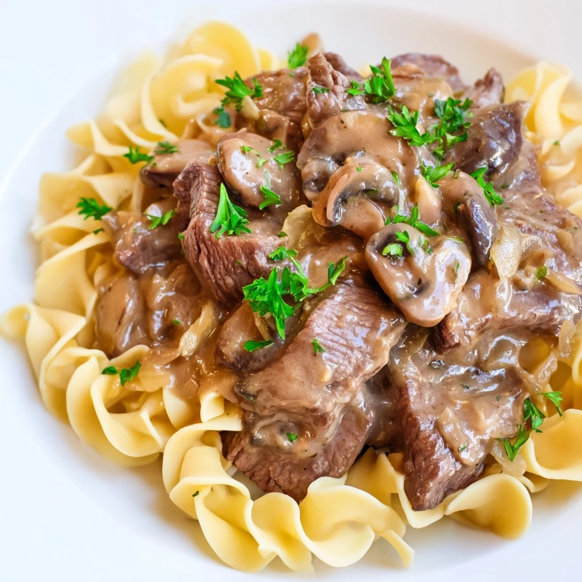 Hearty Beef Stroganoff dinner plated with egg noodles and fresh parsley garnish, highlighting tender beef and savory mushroom sauce.