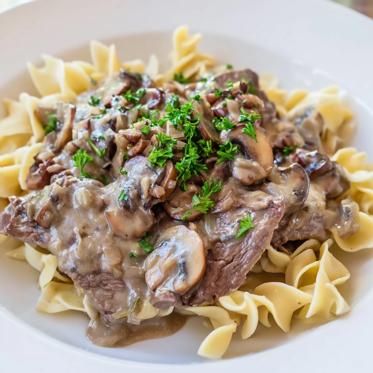 Golden brown beef strips and sliced mushrooms in a rich, creamy gravy served over egg noodles for a comforting Beef Stroganoff.