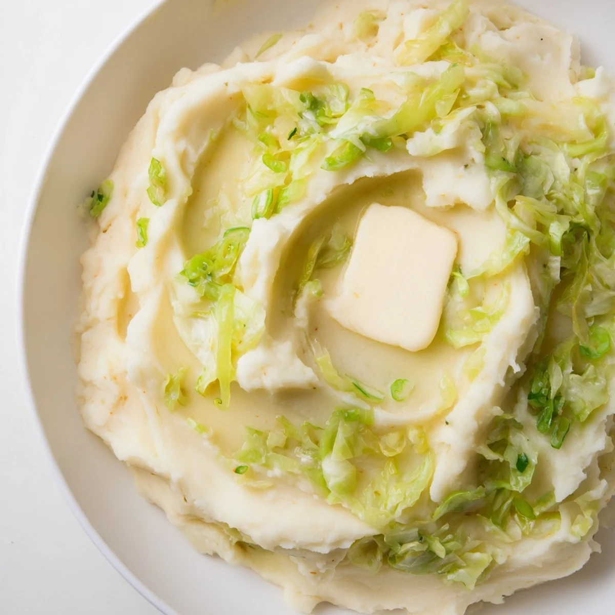 A close-up of buttery St. Patricks Day Colcannon Mashed Potatoes with sautéed greens, ideal alongside corned beef for St. Patrick's Day.