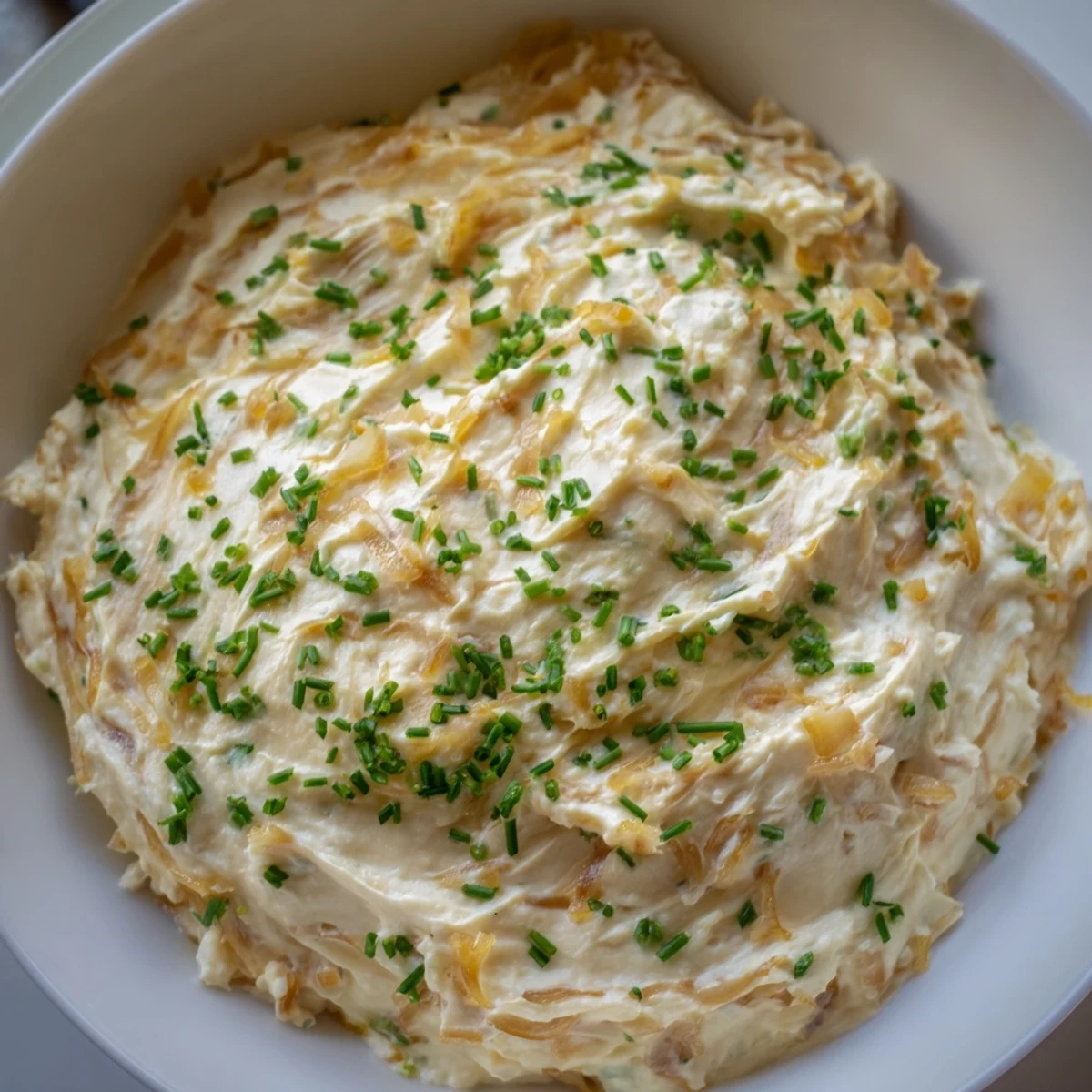 A rustic bowl of homemade Game Day Onion Dip topped with fresh chives, surrounded by crunchy potato chips.