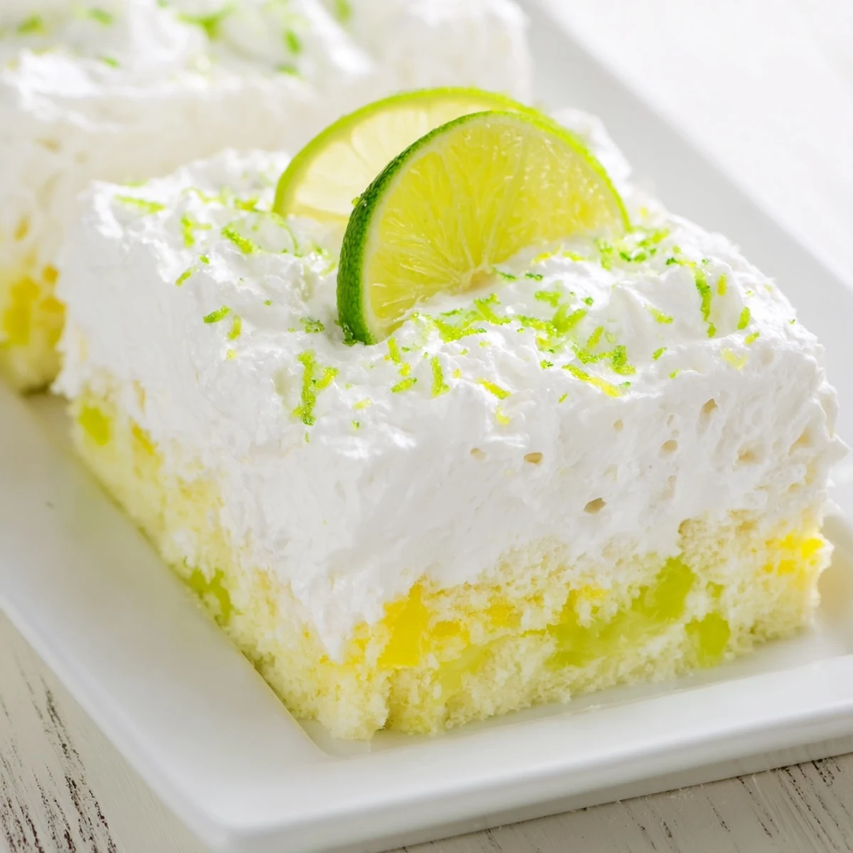 Vibrant green lime poke cake with a fluffy whipped topping and fresh zest garnish.