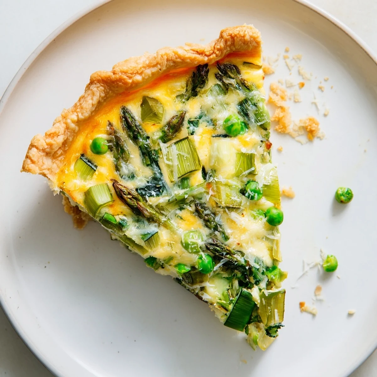 A close-up slice of Spring Vegetable Quiche with Crust, featuring golden-brown pastry, creamy custard, and vibrant green asparagus, zucchini, and peas.