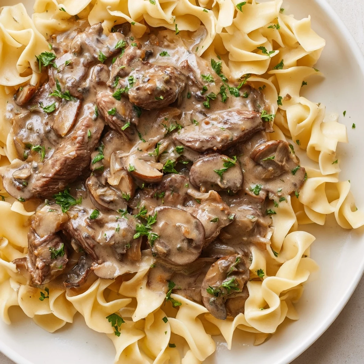 Steaming Beef Stroganoff over Egg Noodles in a creamy mushroom sauce with fresh parsley garnish.
