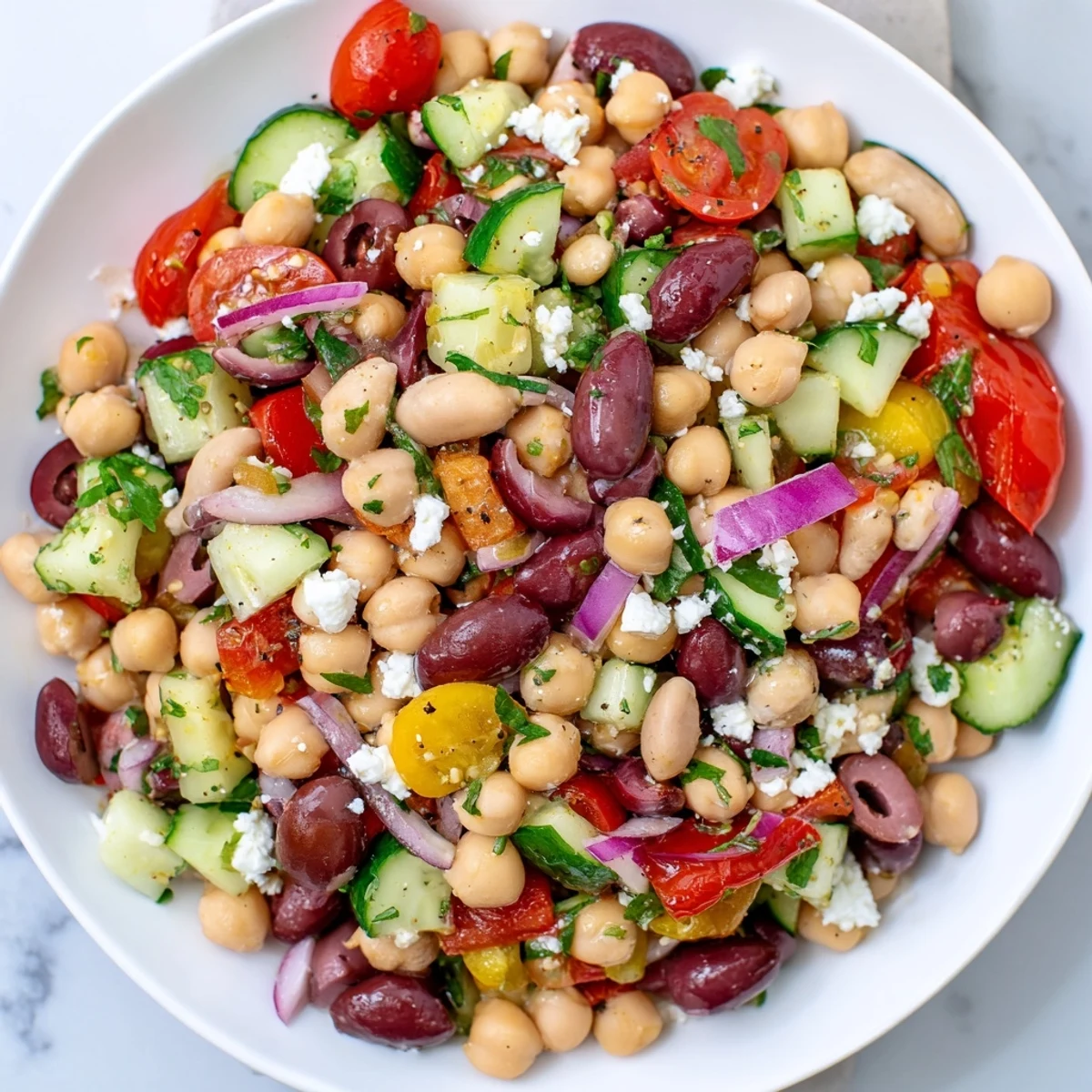 Top-down view of Mediterranean Dense Bean Salad with cherry tomatoes, cucumbers, olives, and fresh herbs tossed in lemony dressing.