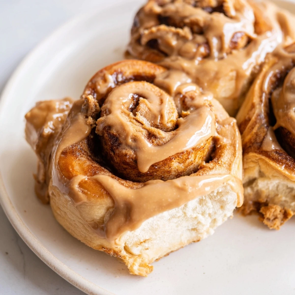 A close-up of Soft and Gooey Biscoff Cinnamon Rolls drizzled with creamy cookie butter icing on a rustic plate.