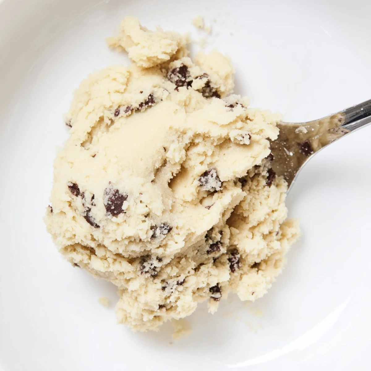 The Edible Keto Cookie Dough shows creamy texture with sugar-free chocolate chips in a white bowl.