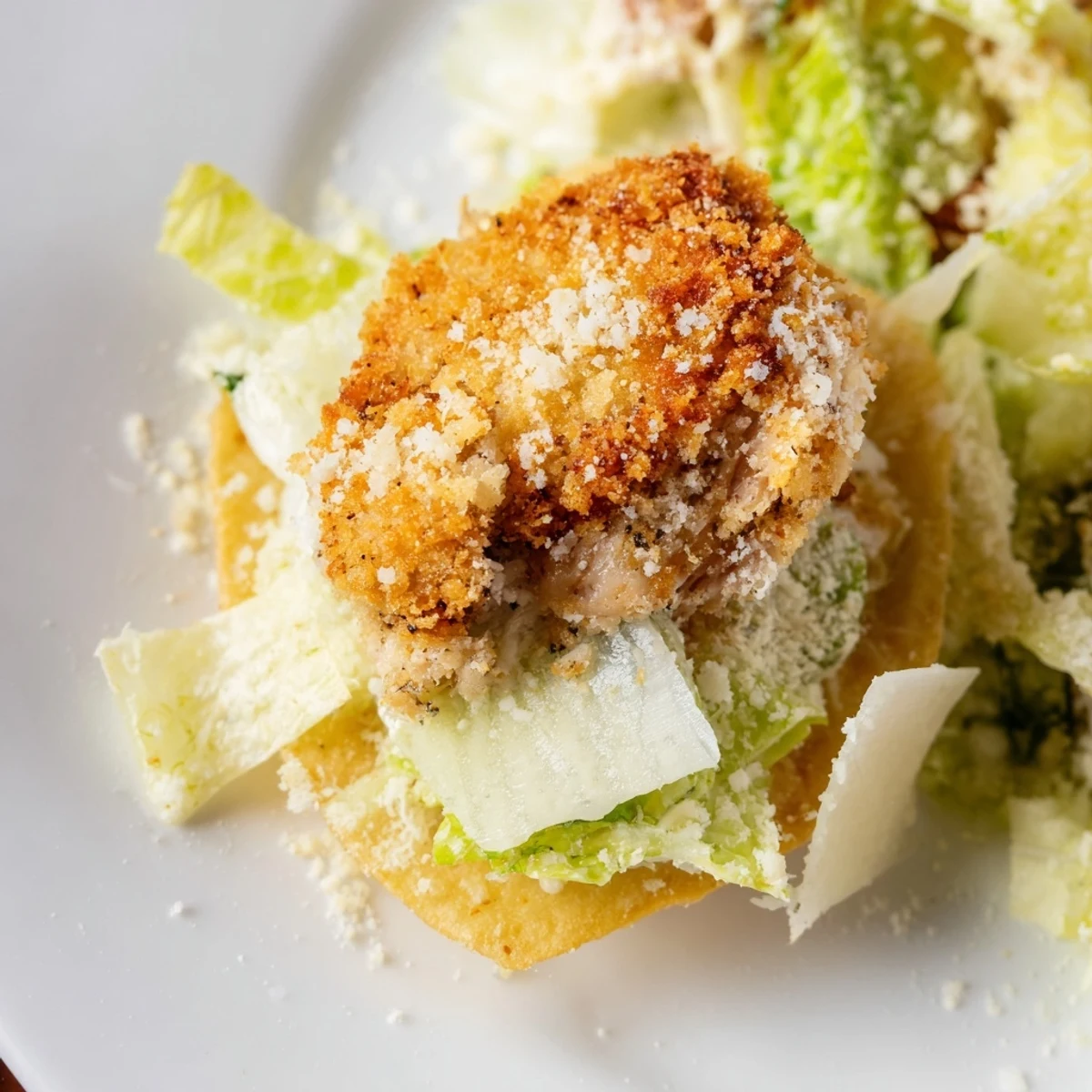 Golden-brown baked potato chips topped with crispy breaded chicken strips, shredded romaine, parmesan shavings, and a creamy Caesar dressing drizzle.