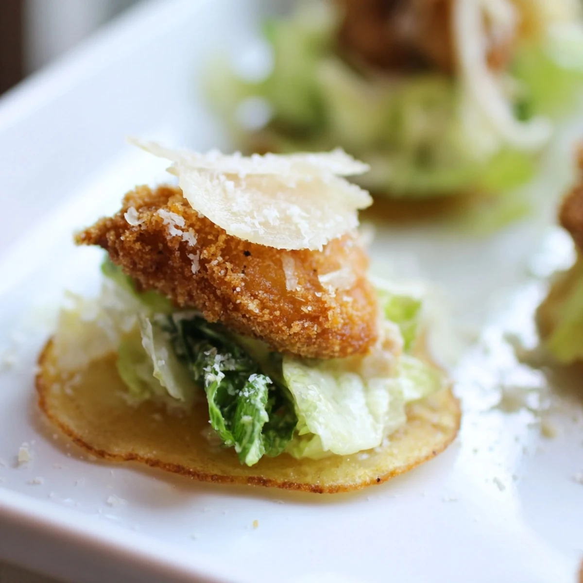 A close-up view of crunchy potato chip bases holding tender chicken pieces, romaine lettuce, and shaved parmesan for a savory snack.