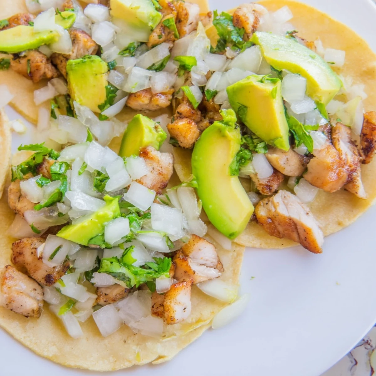 Close-up of golden Chicken Street Tacos topped with crumbled cotija cheese and diced white onion on soft, toasted corn tortillas.