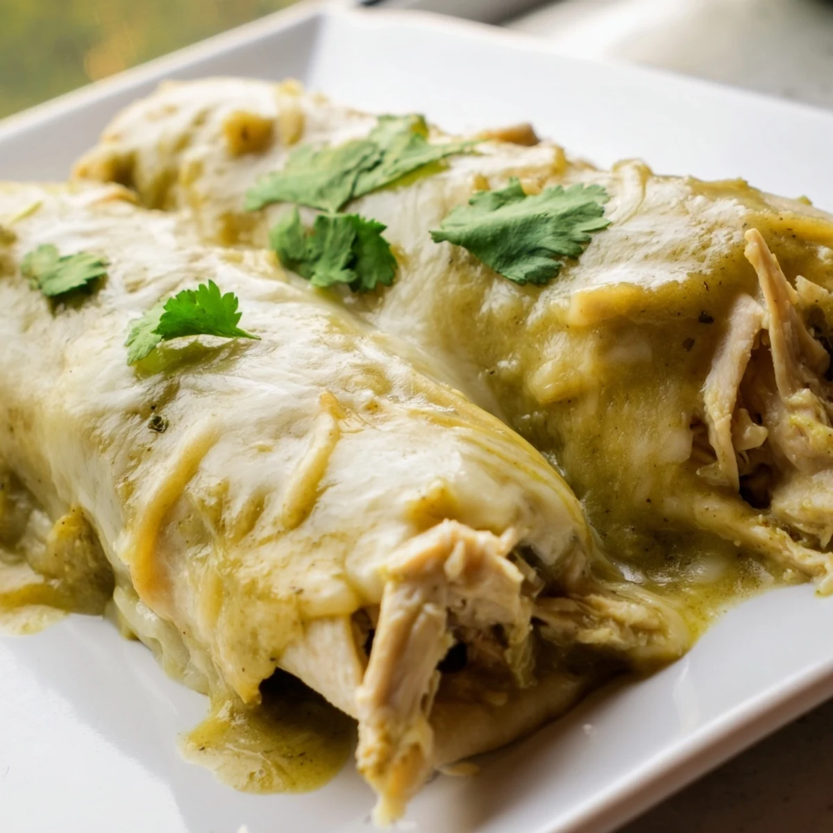 Plated serving of Green Enchiladas With Chicken, drizzled with sour cream and accompanied by sliced avocado.