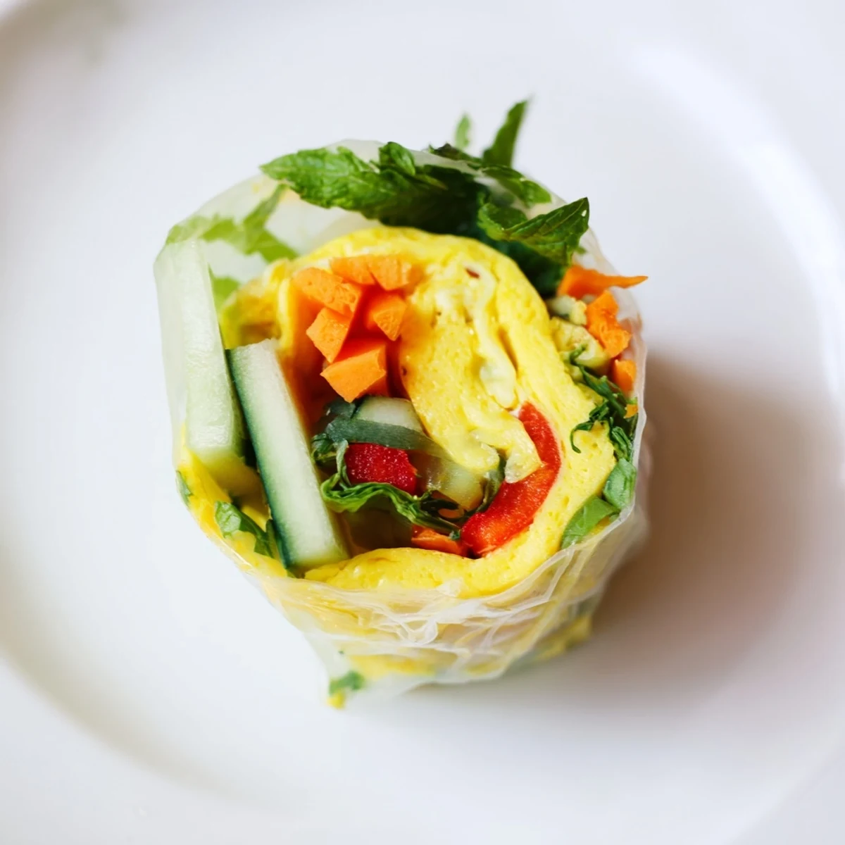 Omelette Spring Rolls are plated with a small dipping bowl of soy sauce, sesame, and ginger, garnished with fresh mint.  