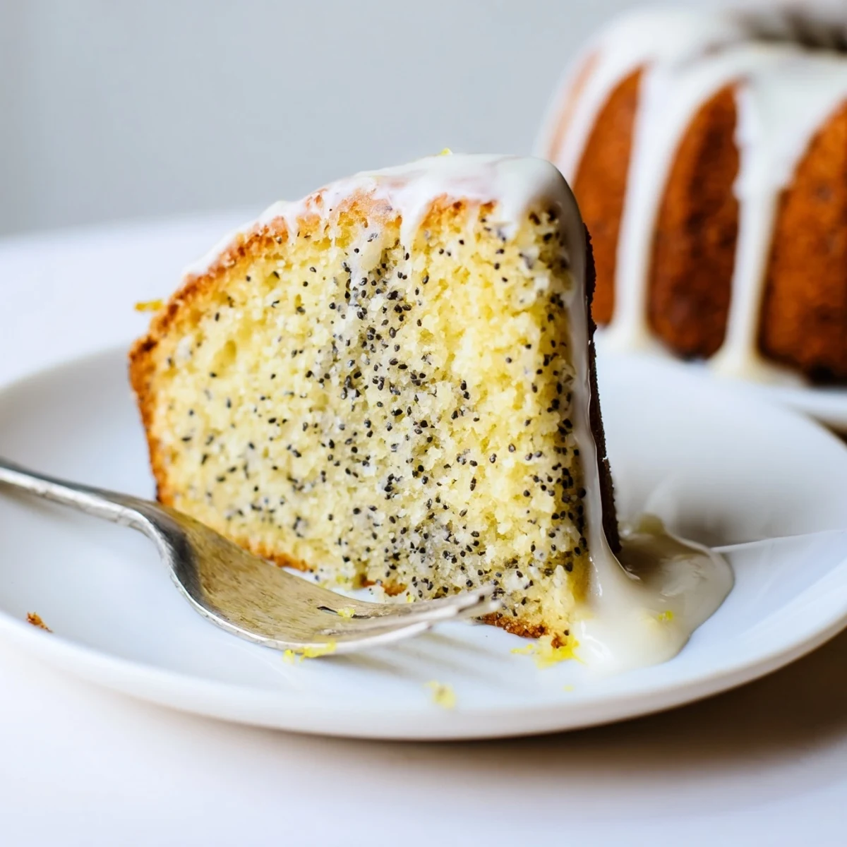 A glazed Lemon Poppy Seed Cake sits on a white ceramic plate with fresh lemon slices nearby for a bright dessert presentation.