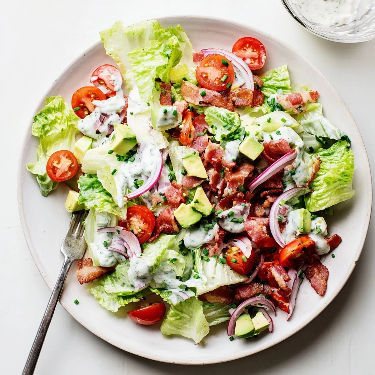 Crispy Bacon Keto BLT Salad arranged on a white plate with crumbled bacon and a drizzle of keto dressing.