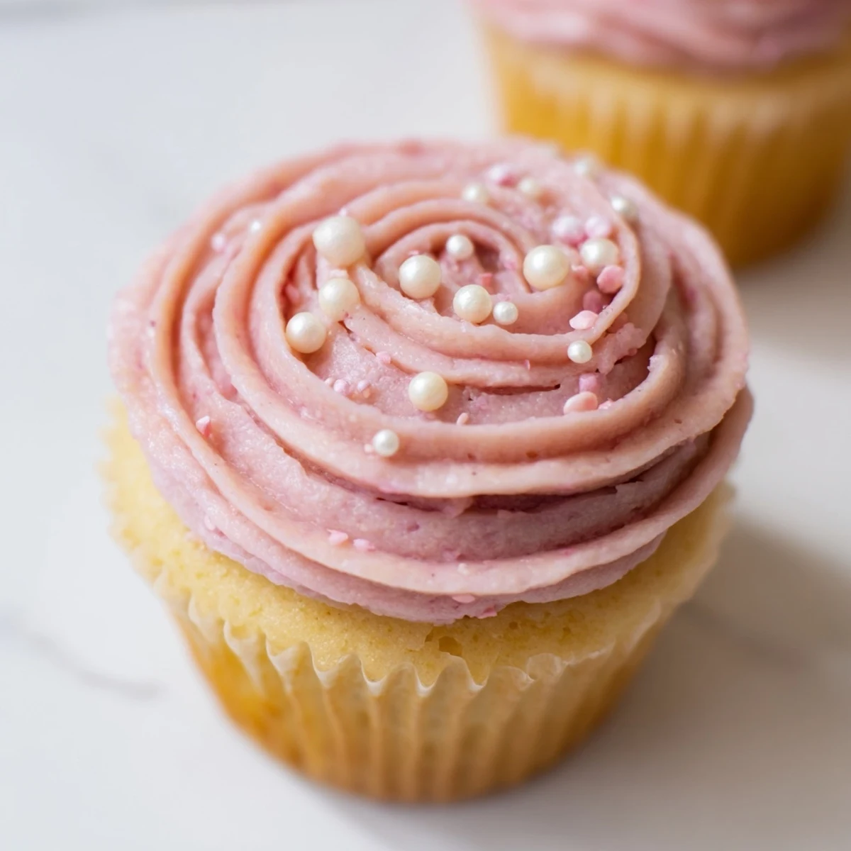 A close-up of Girl Baby Shower Cupcakes with soft pink buttercream swirls topped with edible pearls on a pastel plate.