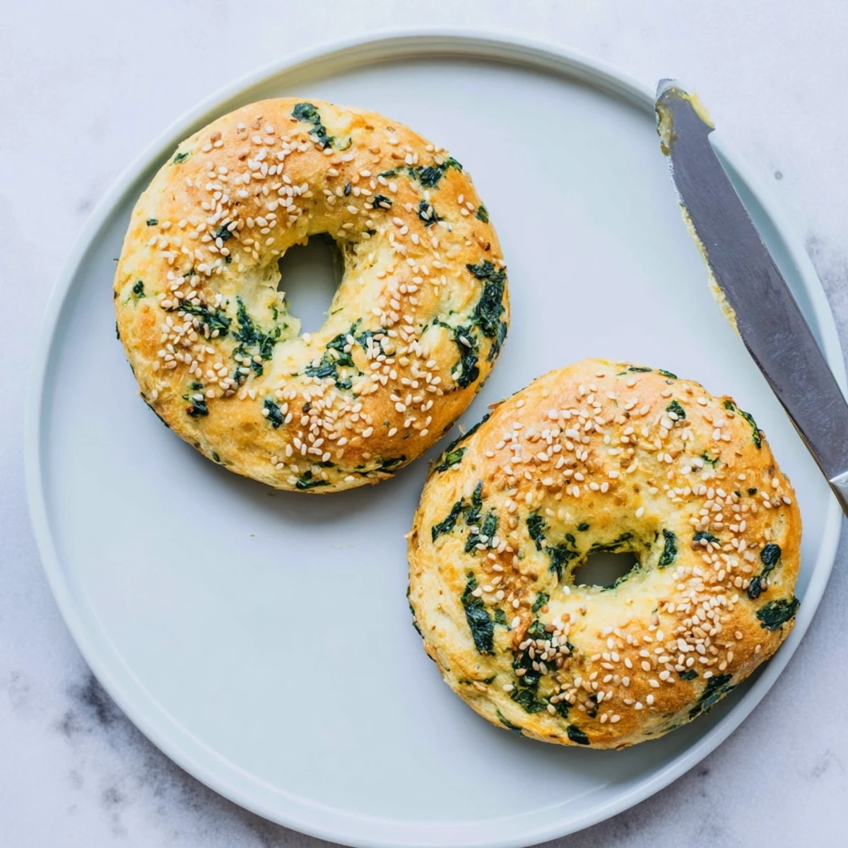 A toasted Spinach Cottage Cheese Flagel spread with butter sits beside a steaming coffee mug on a rustic table.