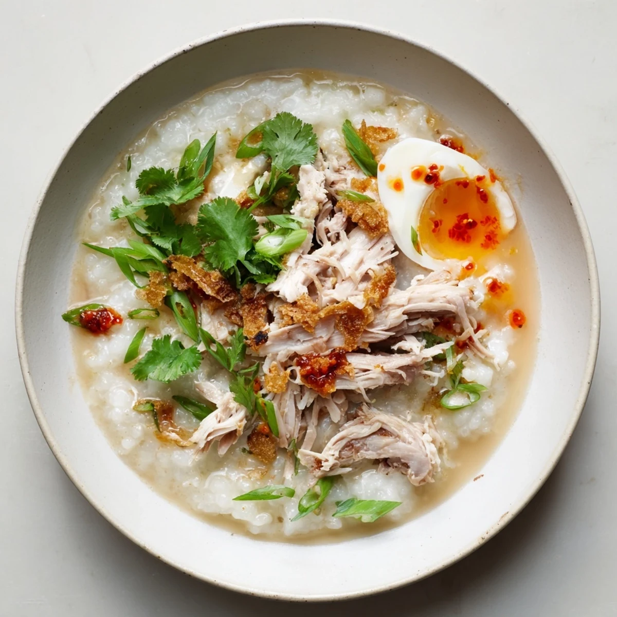 Creamy leftover Thanksgiving turkey congee topped with scallions, cilantro, and crispy shallots in a white bowl