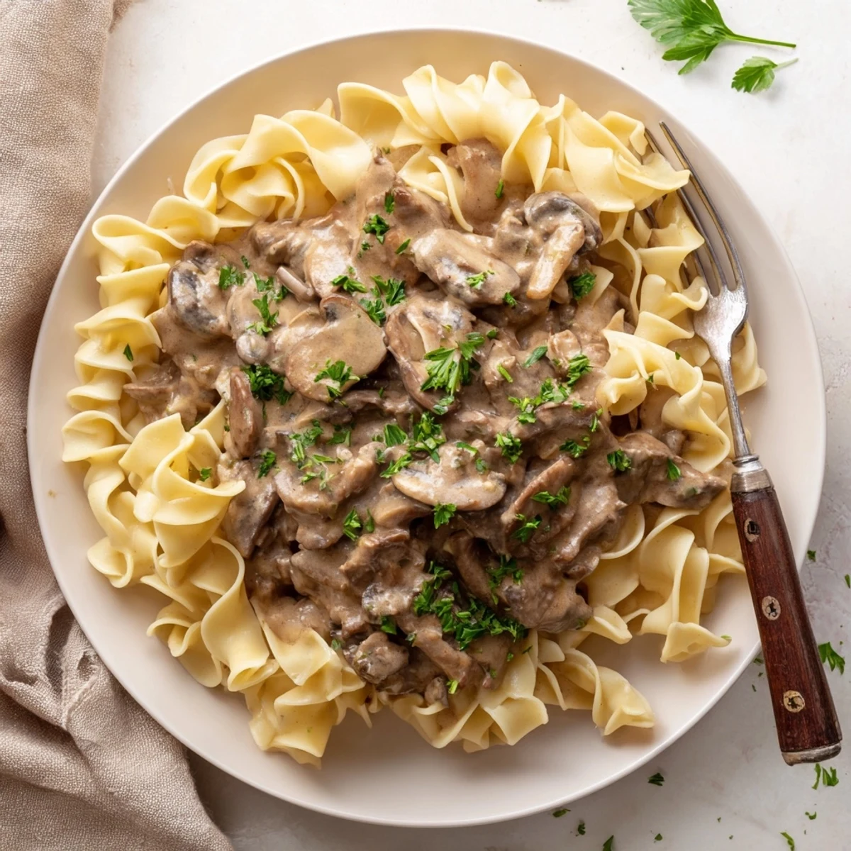 Homemade beef and mushroom stroganoff featuring a velvety sauce ladled over golden egg noodles for a comforting dinner