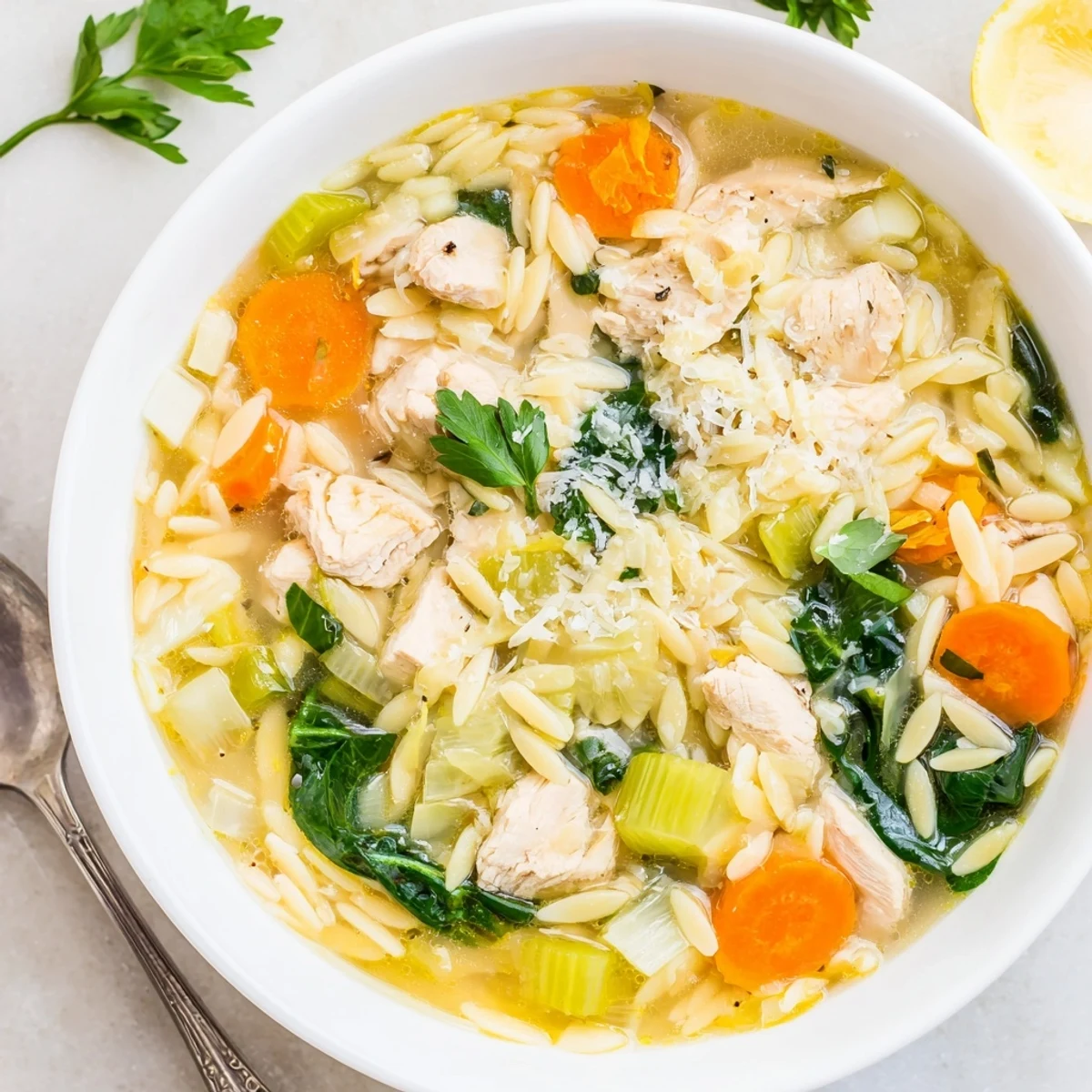 Creamy spring lemon chicken orzo soup with tender vegetables and fresh spinach in a golden broth