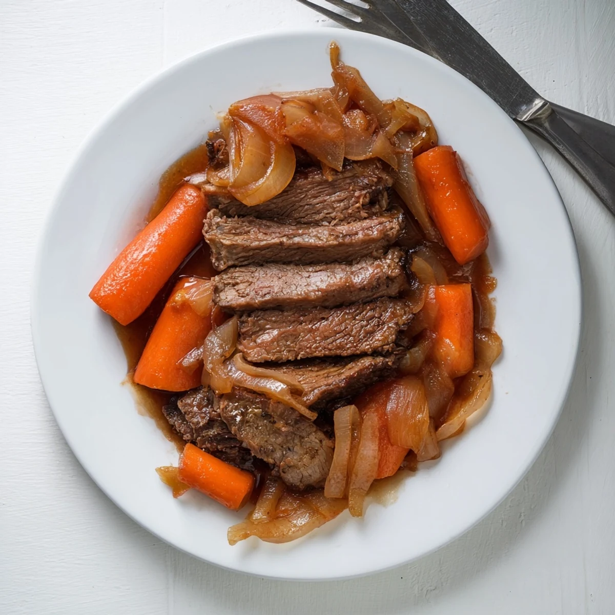 Fork-tender slow cooker beef brisket drizzled with savory dark sauce alongside colorful roasted vegetables on a white serving platter