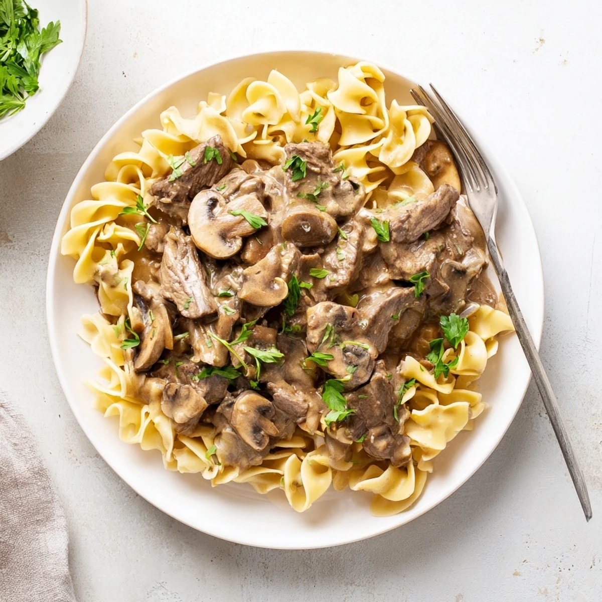 Creamy beef stroganoff plated over wide egg noodles and garnished with fresh chopped parsley
