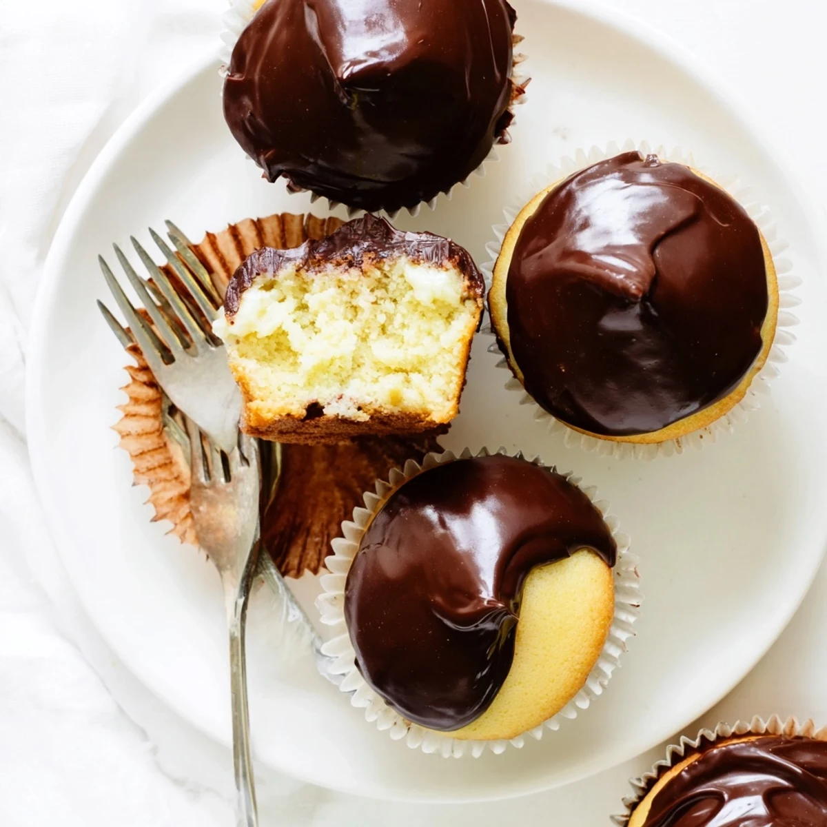 Golden Boston Cream Pie Cupcakes dripping with glossy chocolate ganache over fluffy vanilla cake
