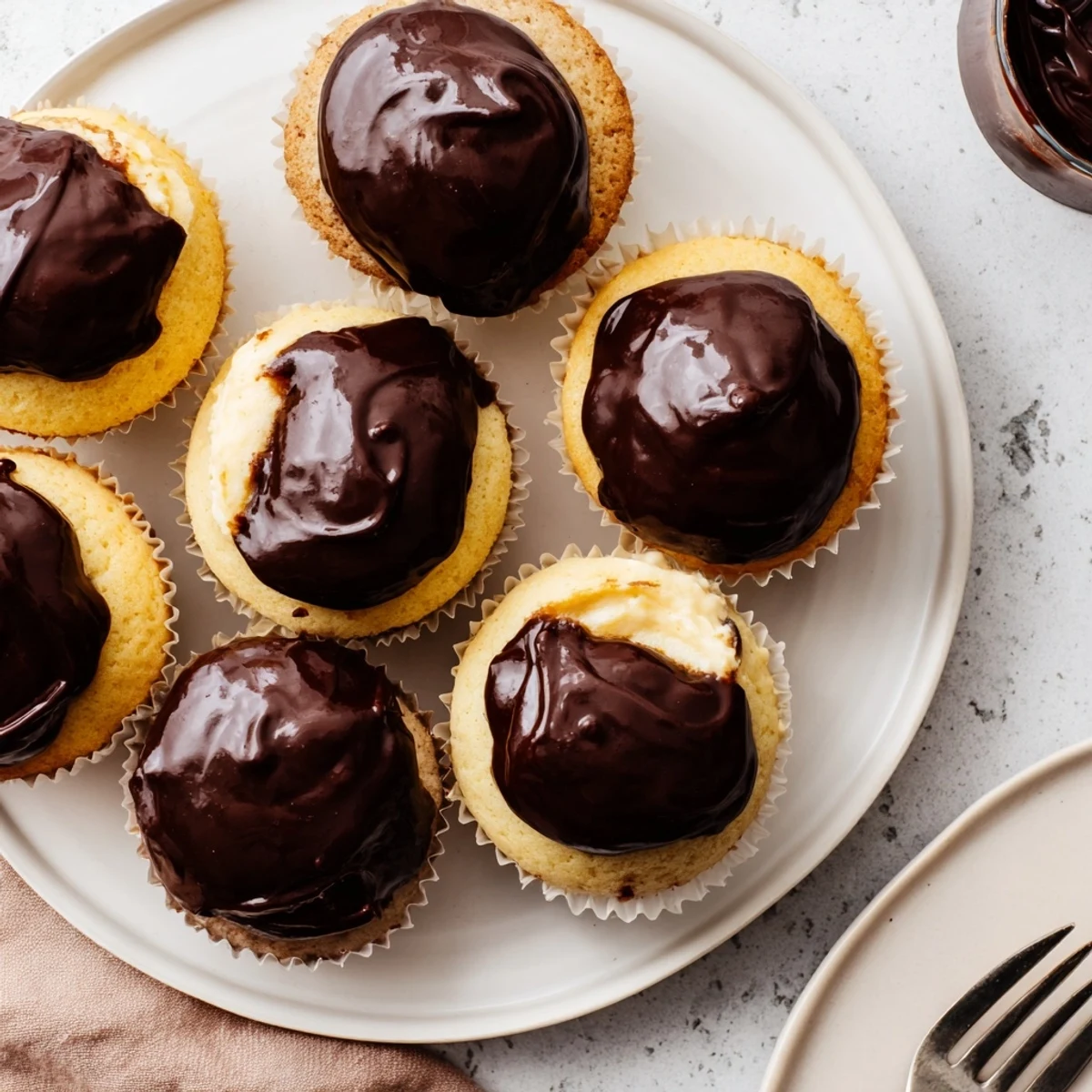 Handheld Boston Cream Pie Cupcakes filled with creamy vanilla custard beneath rich chocolate glaze