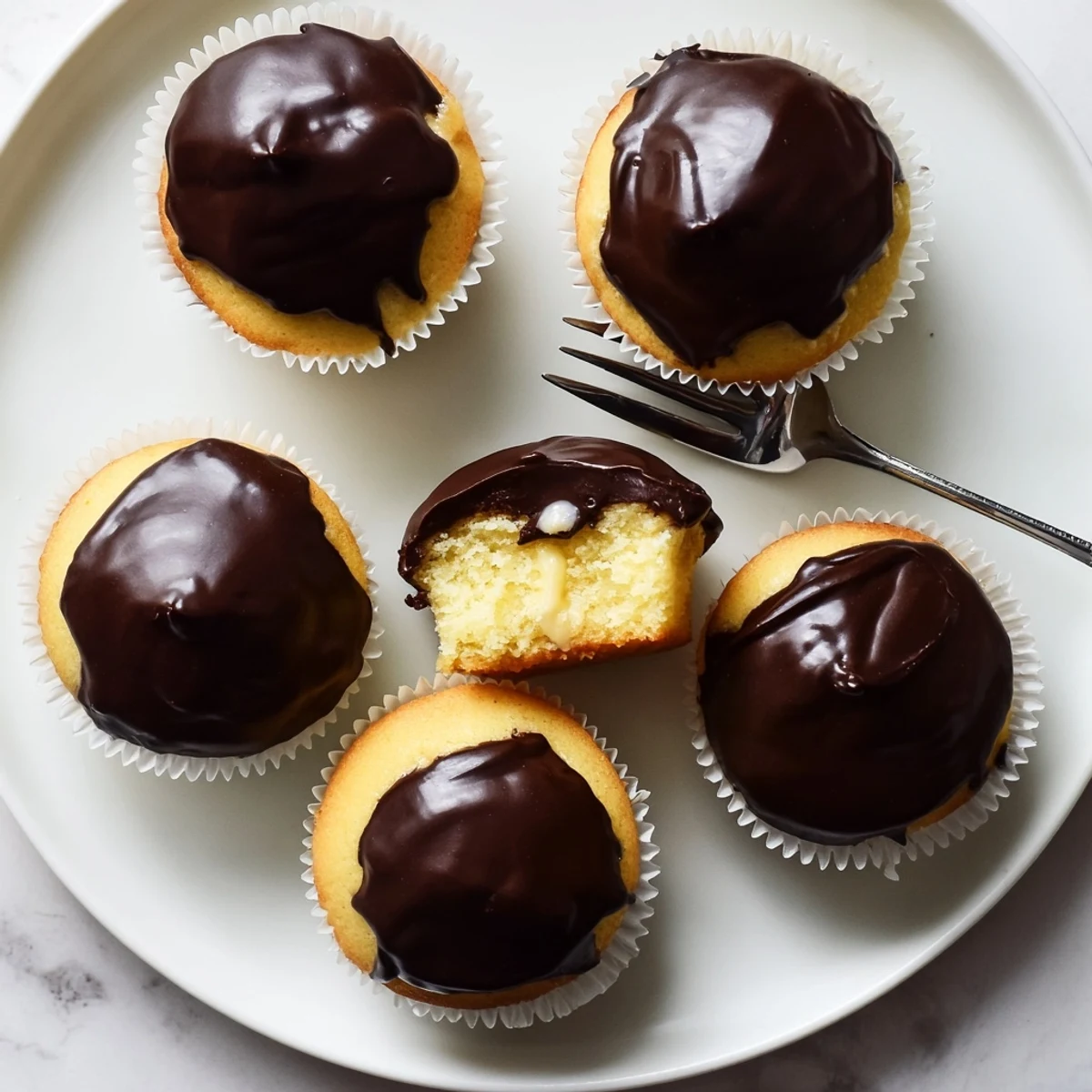 Classic Boston Cream Pie Cupcakes topped with smooth chocolate ganache and filled with pastry cream
