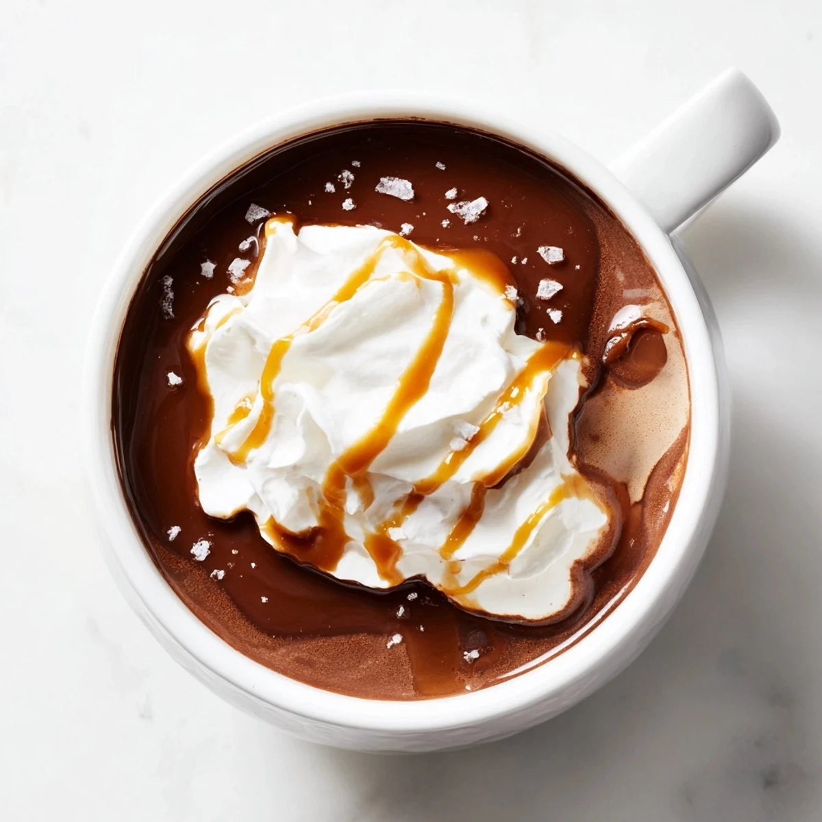Rich salted caramel hot chocolate topped with whipped cream and flaky sea salt in a cozy mug