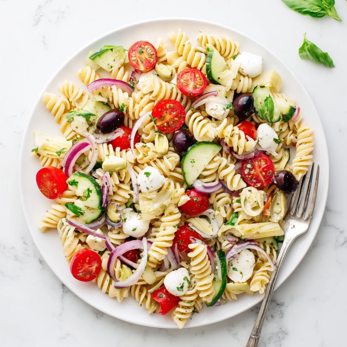 Heaping bowl of chilled Italian vegetarian pasta salad dotted with red bell peppers, cucumber, and creamy mozzarella balls