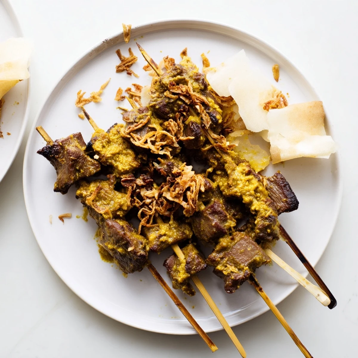 Plate of Indonesian Sate Padang beef skewers smothered in thick aromatic curry sauce beside sliced rice cake