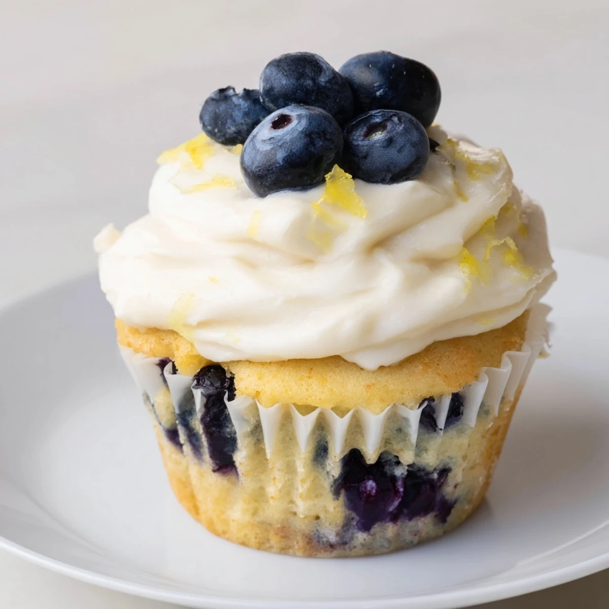 Fluffy lemon blueberry cupcakes topped with tangy cream cheese frosting on a white serving plate