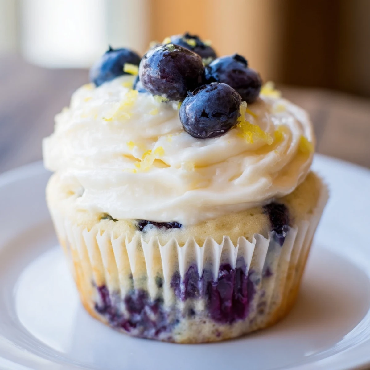 Two frosted lemon blueberry cupcakes with swirling cream cheese topping and fresh blueberry garnish