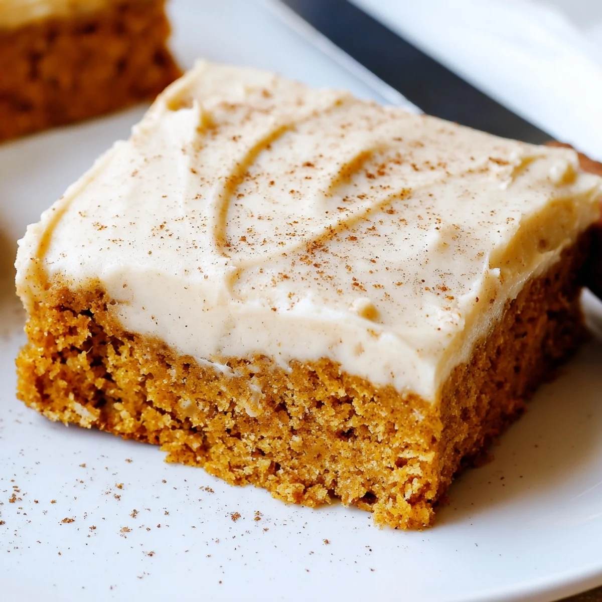 Warm spiced pumpkin bars with thick cream cheese frosting dusted with cinnamon on top