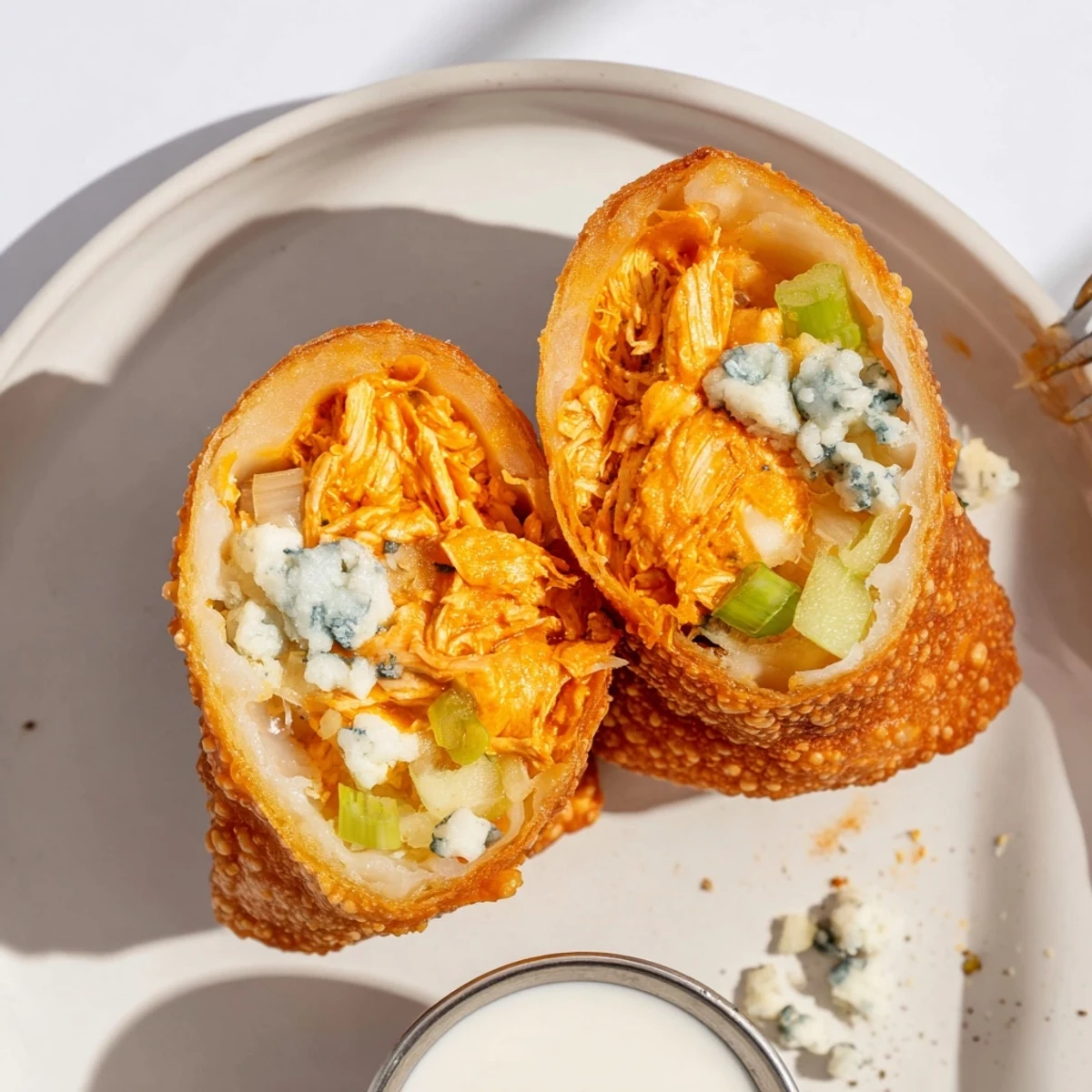 Crispy Buffalo Chicken Egg Rolls oozing cheesy filling beside ranch dipping sauce.