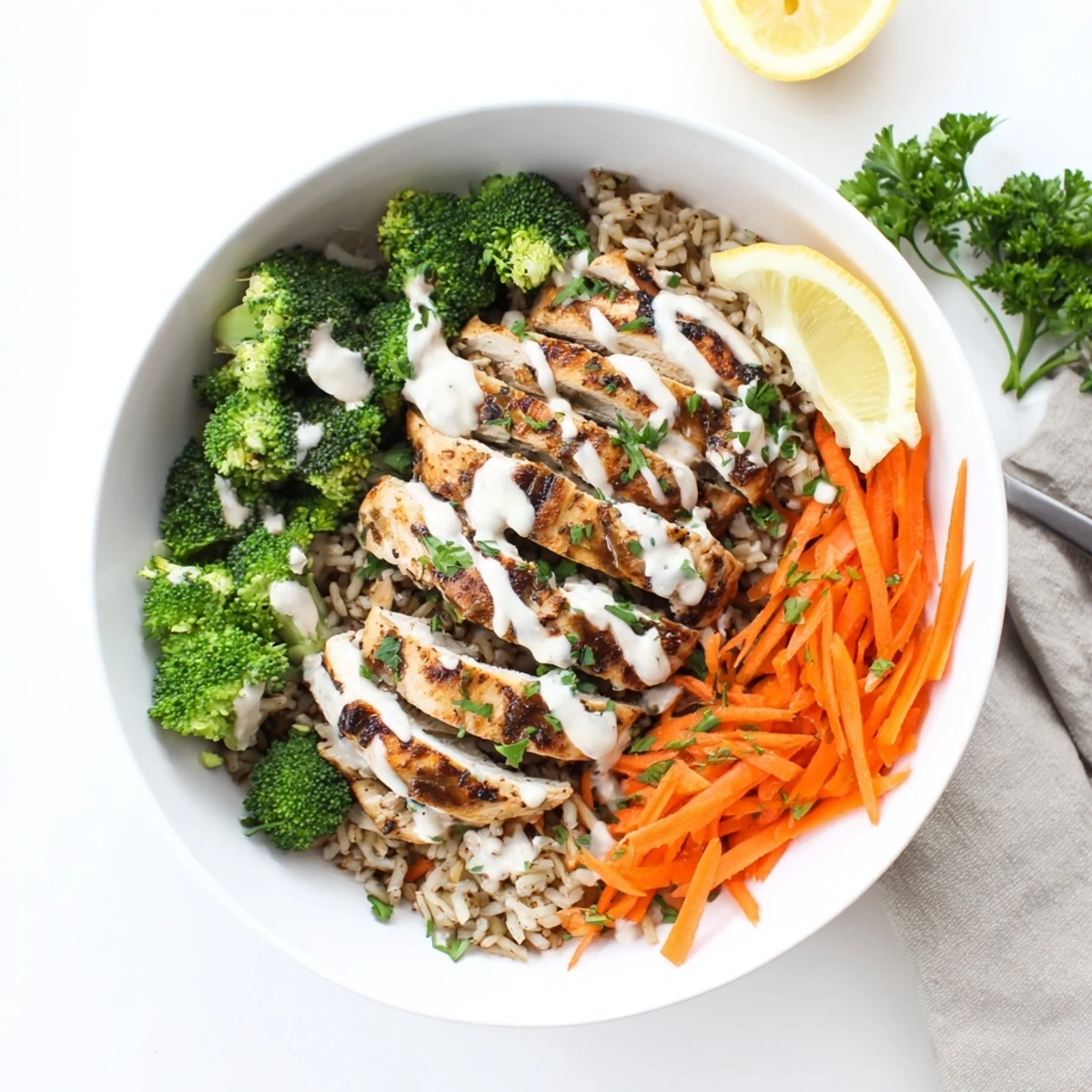 Close up of nutritious grilled chicken and broccoli bowl topped with thick creamy garlic dressing and lemon wedges