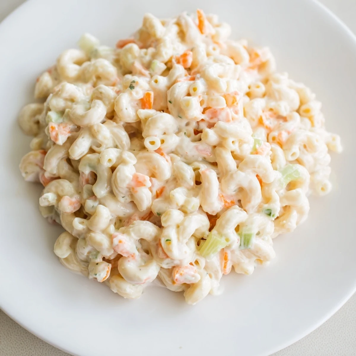 Vibrant Hawaiian style mac salad plated as a side dish beside grilled teriyaki chicken highlighting the signature creamy coating and tender overcooked pasta