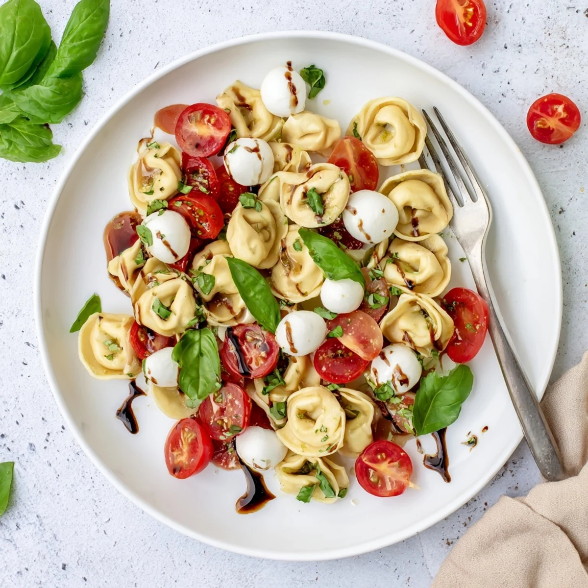 Fresh tortellini Caprese salad drizzled with balsamic glaze alongside halved cherry tomatoes