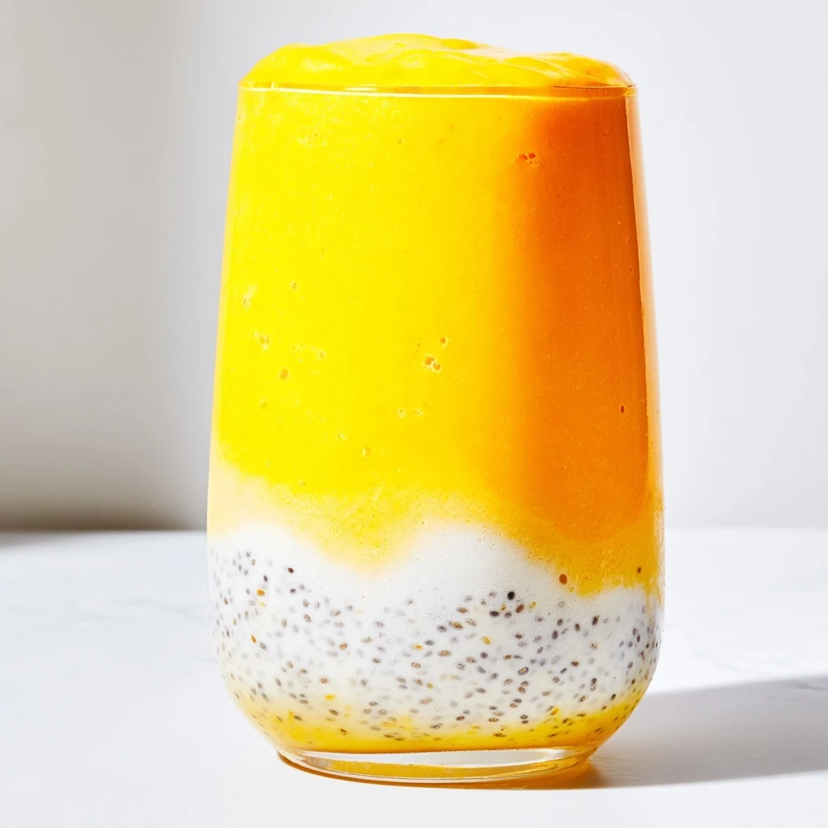 Creamy orange-yellow Tropical Sunrise Protein Smoothie topped with chia seeds and pineapple slice