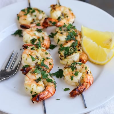 Golden grilled lemon garlic shrimp skewers served on a white plate with lemon wedges for squeezing.
